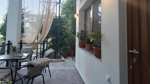 A covered outdoor seating area with a table and chairs, potted plants, and a view of the surrounding area. - Isidora Apartments (Zagora-Mouresi)