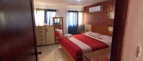 Ein Schlafzimmer mit einem Bett, einem Kleiderschrank, einem Spiegel und einer Wandklimaanlage.