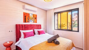 Une chambre d’hôtel avec un grand lit, une tête de lit rouge, une fenêtre donnant sur un beau paysage et un tableau accroché au mur.