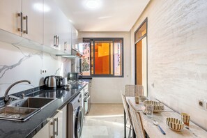 A modern kitchen with a marble backsplash, stainless steel appliances, and a dining area with a table and chairs. - Fabulous 2-Bedroom Apartment with AC in Marrakech City Center (Marrakech)