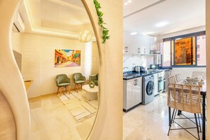 A modern kitchen with a washing machine, dining area with chairs, and a painting on the wall. - Fabulous 2-Bedroom Apartment with AC in Marrakech City Center (Marrakech)