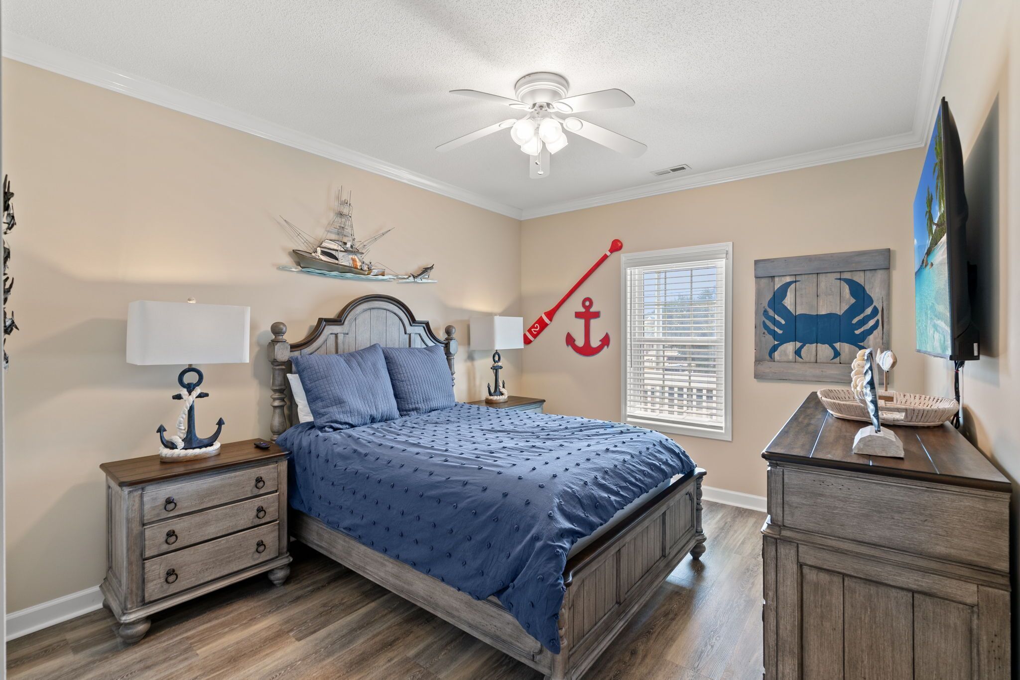 A bedroom with a bed, nightstands, a dresser, a ceiling fan, and nautical-themed decor.