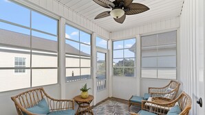 Uma sala de sol com móveis de vime, grandes janelas e um ventilador de teto.