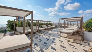 Eine Dachterrasse mit Liegestühlen und einem gemusterten Boden mit Blick auf eine Stadtlandschaft.