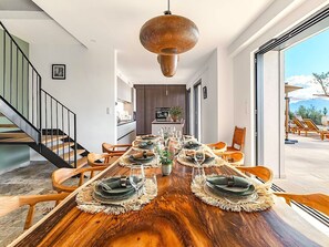 A dining area with a wooden table set for six, a kitchen in the background, and a staircase leading to another level. - Villa Paolina (Olmeto)