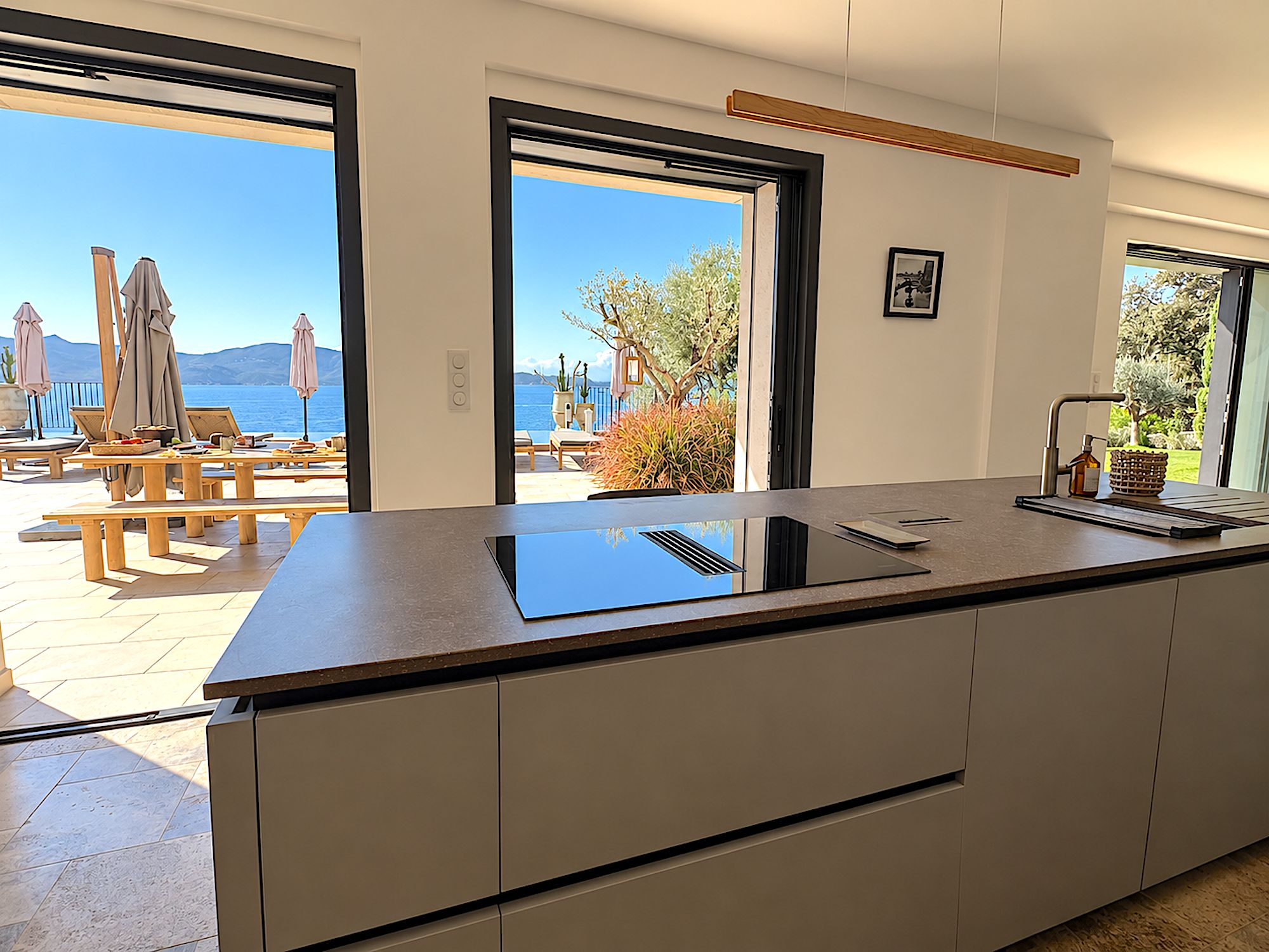 A modern kitchen with a large island, a view of the sea, and outdoor seating.