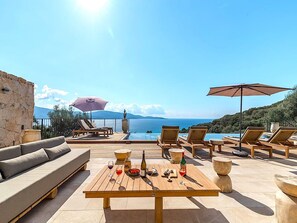 A terrace with lounge chairs, a table with drinks, and a view of the sea and mountains. - Villa Paolina (Olmeto)