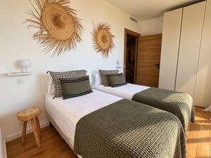 Ein Doppelzimmer mit zwei Betten, einem Holzschrank und einem kleinen Hocker.