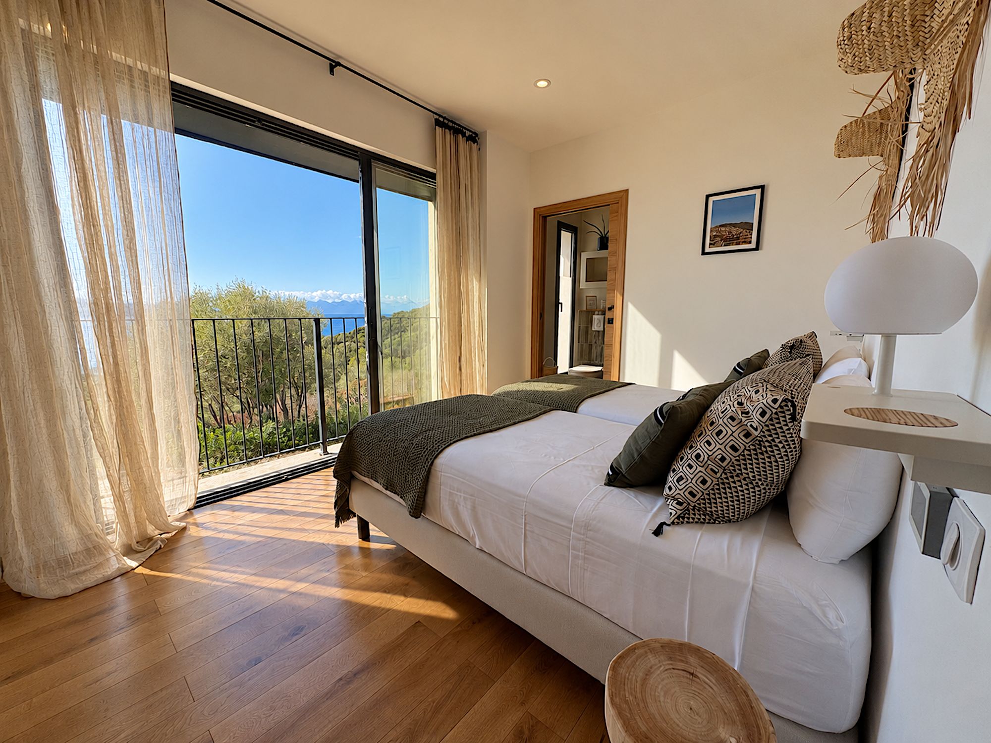 A bedroom with a large bed, a view of the outdoors, and a wooden floor.