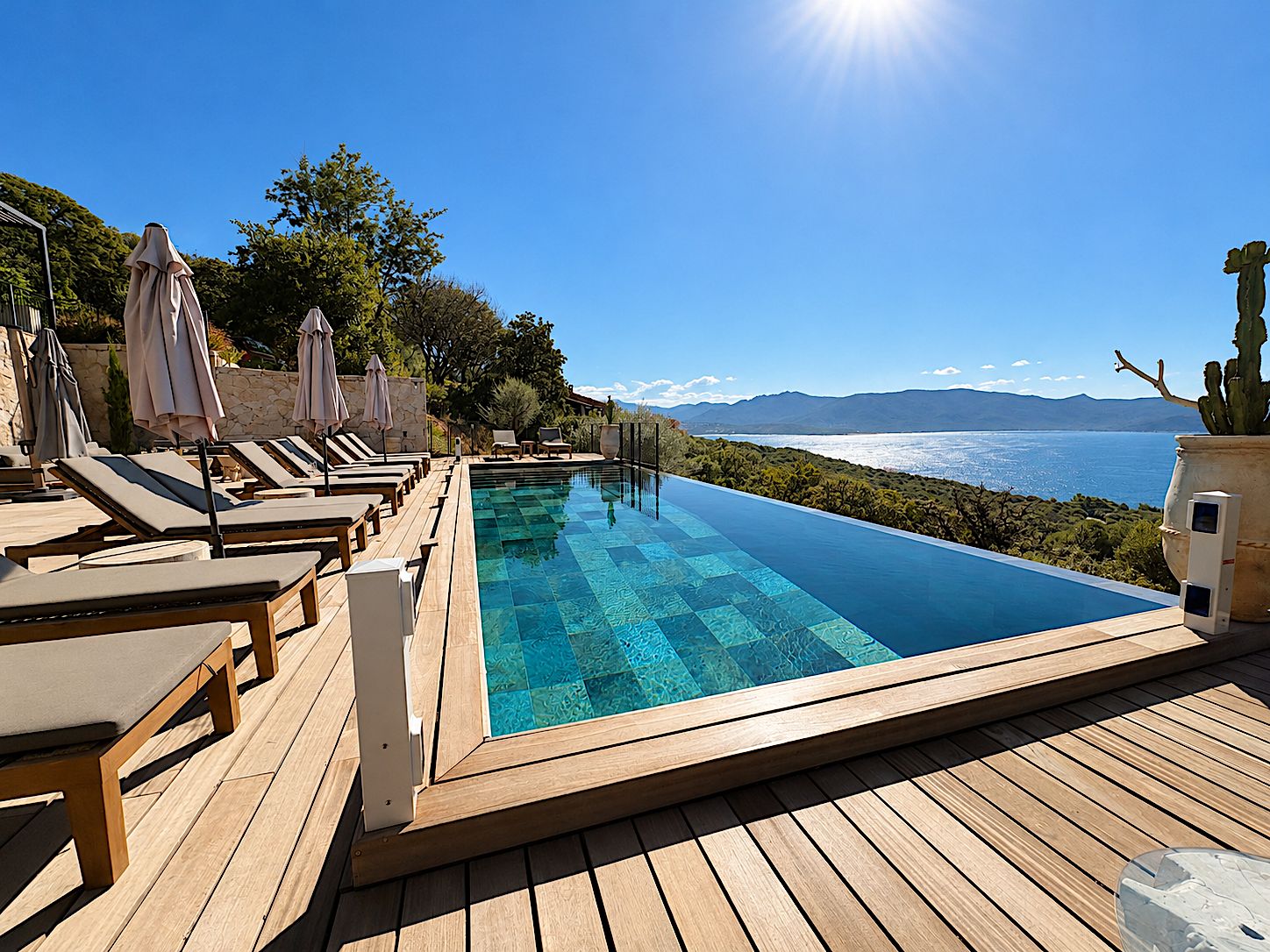 Ein Fernblick über eine Küstenlandschaft auf einen Pool im Freien mit Liegestühlen und Sonnenschirmen.