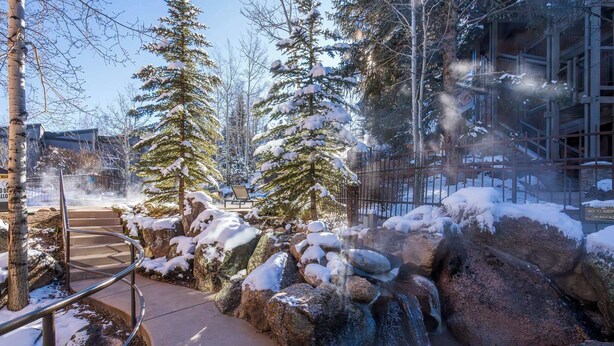 A snow-covered outdoor area with a hot tub, a waterfall, and a staircase leading to a building. - New Ski-in Ski-out 1 BR with Resort Amenities (Snowmass Village)
