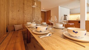 Un'area pranzo con un tavolo di legno lungo apparecchiato per un pasto, con piatti, ciotole e bicchieri da vino bianchi.