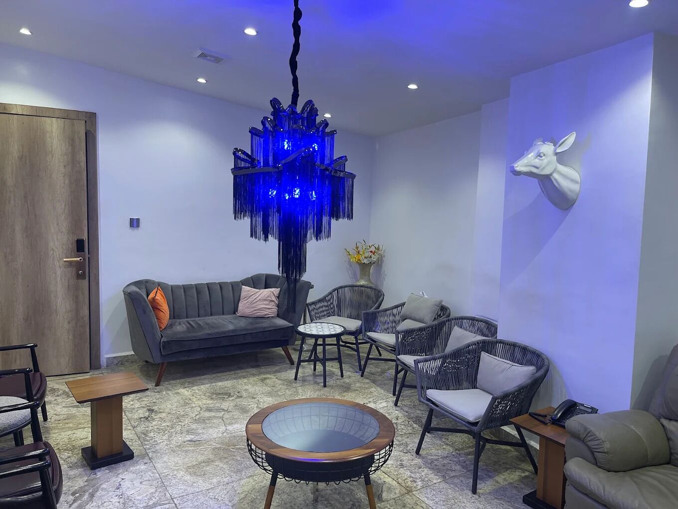 A modern living room with a grey sofa, wicker chairs, a round coffee table, and a unique blue chandelier.