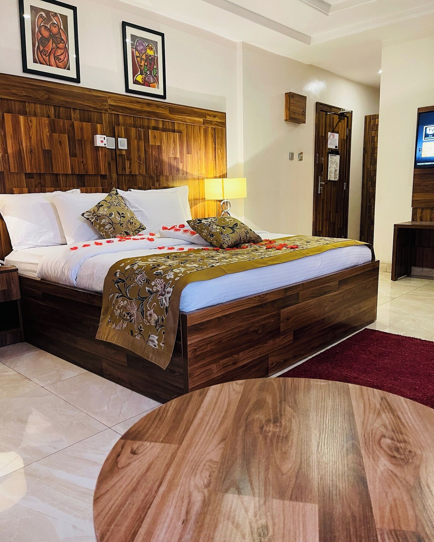 A hotel room with a wooden bed, a round table, and a TV on the wall.