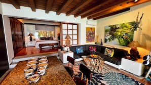 A living room with a sofa, coffee table, and chairs, a dining area with a table and chairs, and a large window with blinds. - Waterfront Condo in Magnificent Manzanillo Bay Troncones (Troncones)