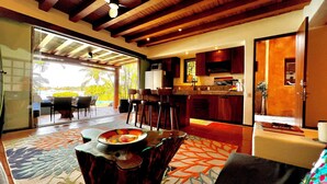 A spacious living area with a dining table, kitchen, and large sliding glass doors leading to a balcony with a view. - Waterfront Condo in Magnificent Manzanillo Bay Troncones (Troncones)