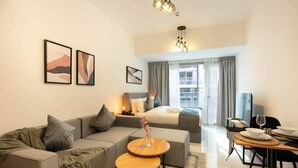 Una habitación de hotel moderna con sofá, una mesita redonda, cama con vistas y zona de comedor con mesa para dos.