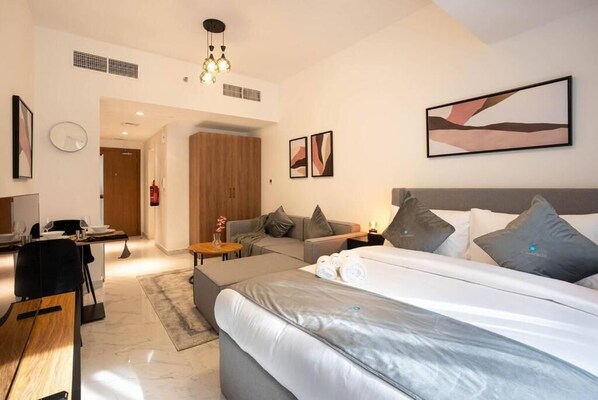 A modern hotel room with a large bed, a desk, and a sofa. There are two framed artworks on the wall and a fire extinguisher near the door. - Bloomfields Spacious STU in Oasis Ma (Abu Dhabi)