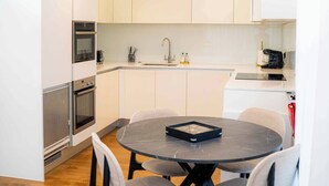 Une cuisine moderne avec des armoires blanches, un four encastré et un coin repas comprenant une table ronde et quatre chaises.