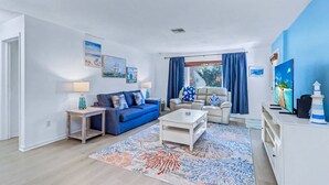 Una sala de estar moderna con un sofá azul, una mesa de centro blanca y un televisor sobre un mueble blanco.