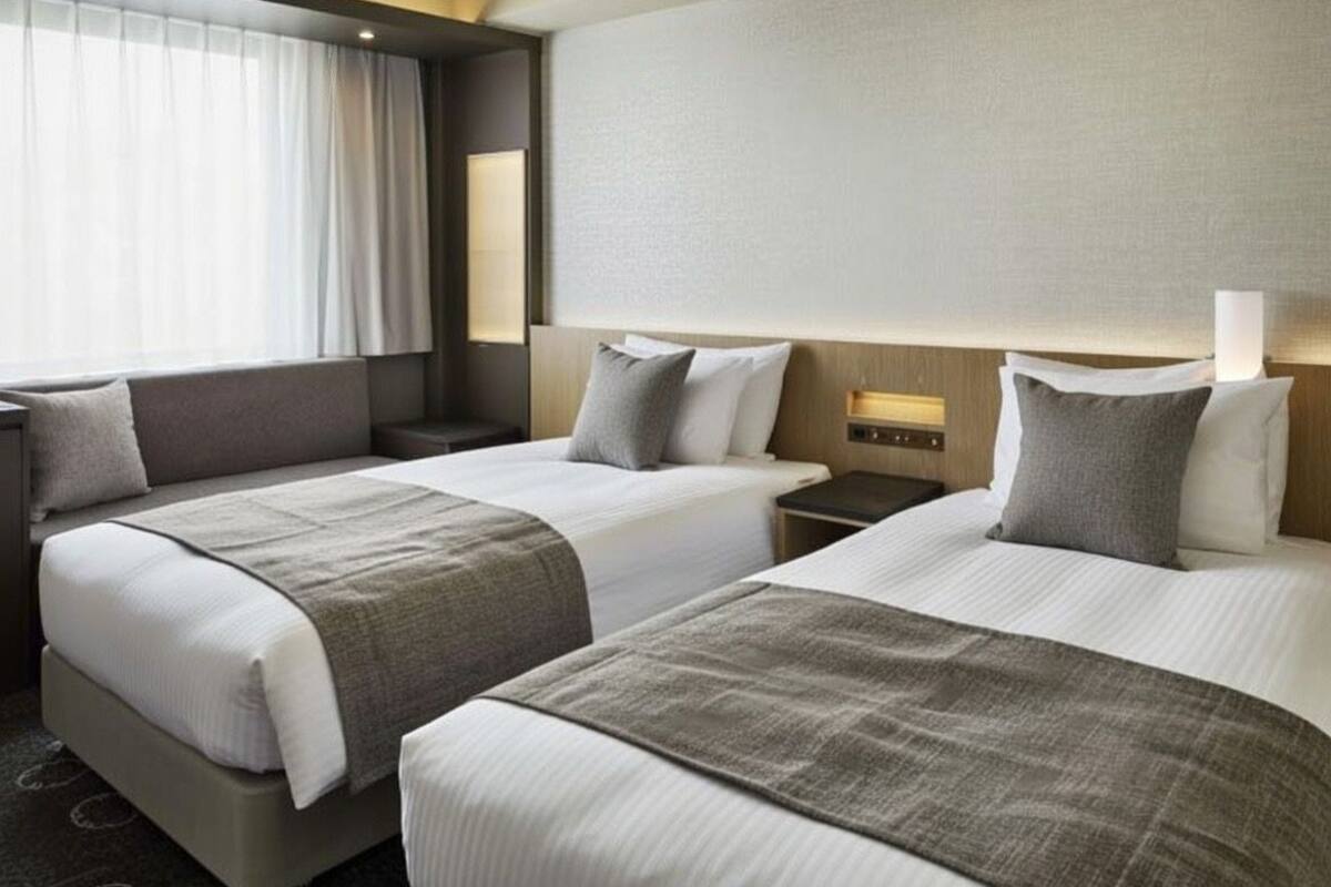 A hotel room with two beds, a nightstand, a lamp, and a window with curtains.