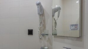 Un bany amb un assecador de cabells fixat a la paret, un mirall i un petit safataire.