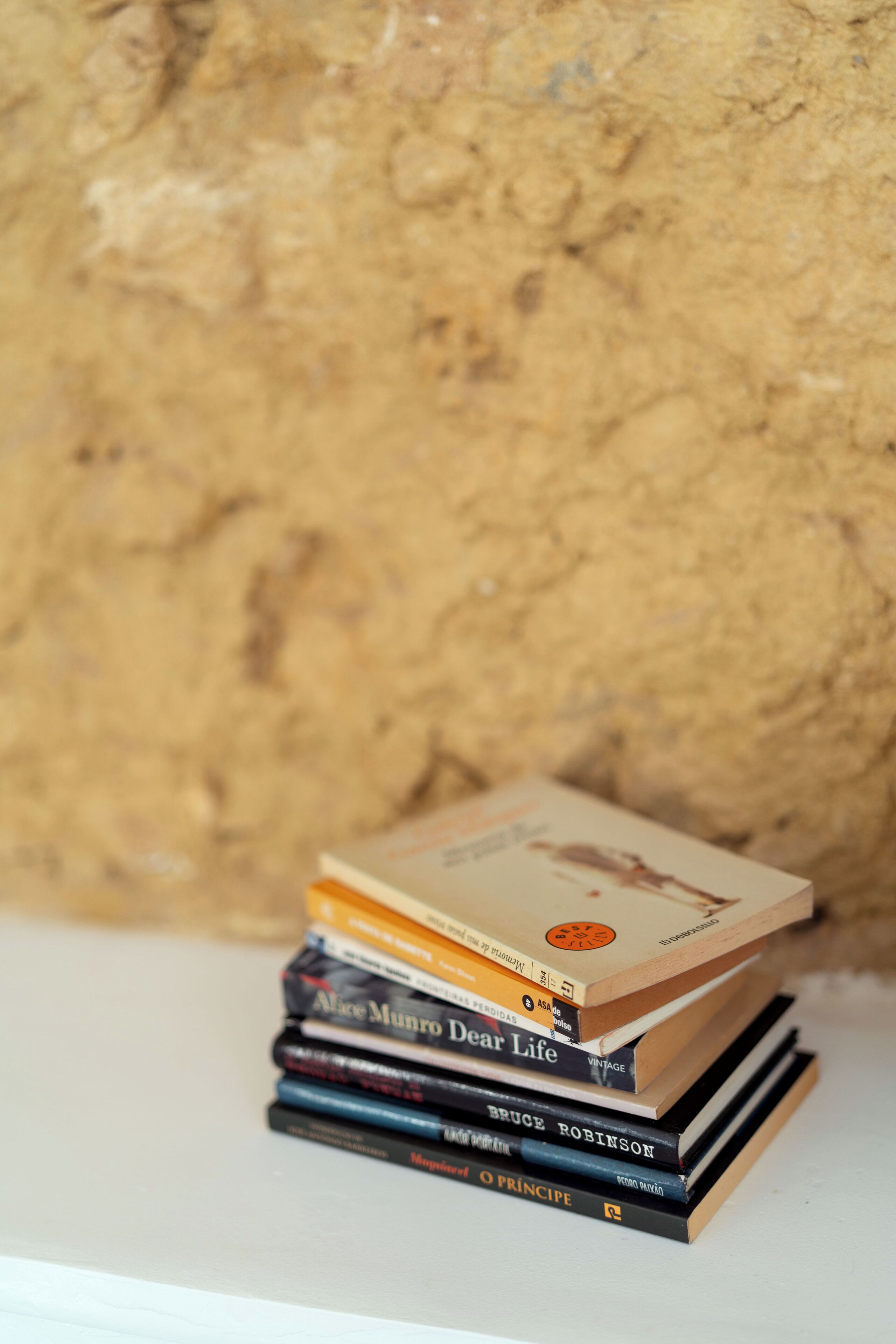 A stack of books on a white surface against a textured wall.