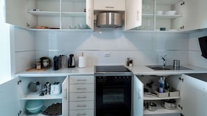 A modern kitchen with white cabinetry, a built-in oven, a stainless steel range hood, and a sink.