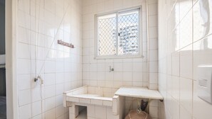 Ein kleines Badezimmer mit Fliesen, einem Fenster, einem Waschbecken und einem Handtuch, das an der Wand hängt.