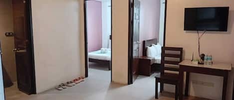 A hotel room with a bed, a desk, a chair, a TV, and a pair of slippers on the floor.
