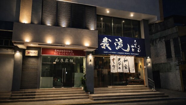 Un bâtiment moderne avec une enseigne indiquant « SHANDONG RESIDENCES » et « GARFU, restaurant proposant une authentique cuisine japonaise ».