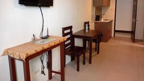 Une petite pièce bien éclairée, comprenant une table à manger, des chaises, un téléviseur fixé au mur et un coin cuisine.