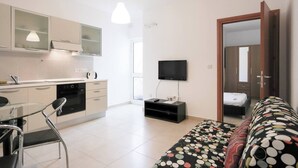 A compact living space with a kitchenette, a dining area with a chair, a bed with a colorful blanket, and a TV mounted on the wall. - Enjoy a stylish 1-bedroom apartment in the heart of Sliema, just steps from the promenade, beaches, cafés, and bus stops. Fully equipped with Wi-Fi, air conditioning, and kitchen — ideal for couples or small families visiting Malta. (Tas-Sliema)