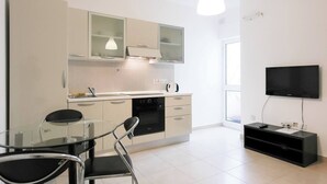 A modern kitchen with a dining area, a TV, and a black entertainment unit. - Enjoy a stylish 1-bedroom apartment in the heart of Sliema, just steps from the promenade, beaches, cafés, and bus stops. Fully equipped with Wi-Fi, air conditioning, and kitchen — ideal for couples or small families visiting Malta. (Tas-Sliema)