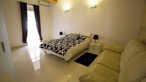 A bedroom with a bed, bedside tables, a sofa, and a window with curtains. - Valletta-Central duplex maisonette (Valletta)