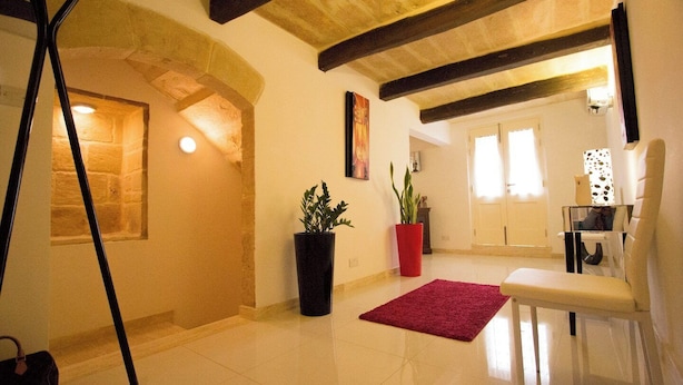 A spacious living area with a high ceiling, exposed beams, a red rug, and a white chair. - Valletta-Central duplex maisonette (Valletta)