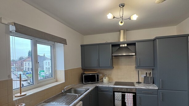 Een moderne keuken met grijze kastjes, een ingebouwde wasmachine, een magnetron en een raam met uitzicht op de stad.