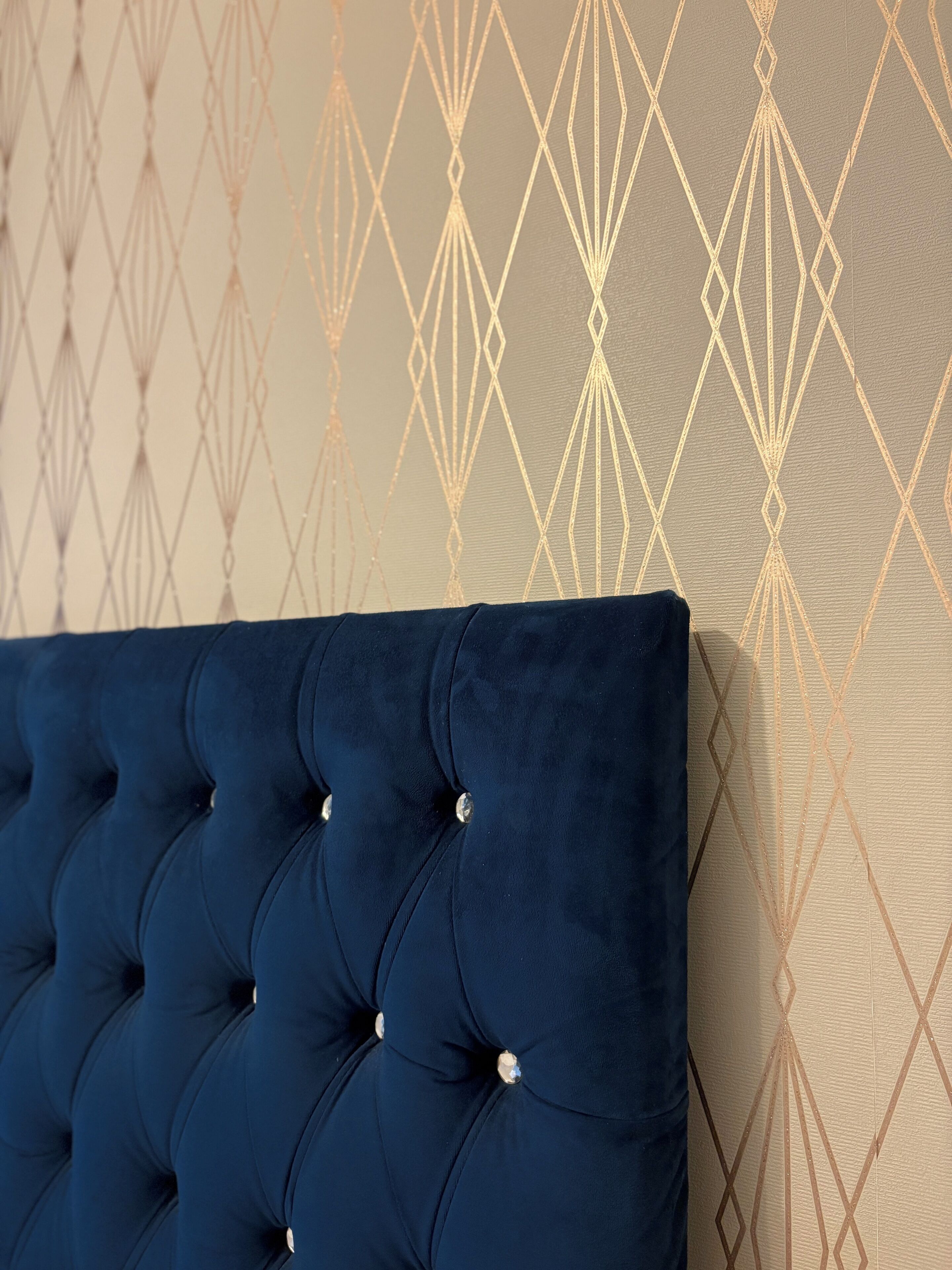 A tufted headboard with a geometric pattern on the wall behind it.