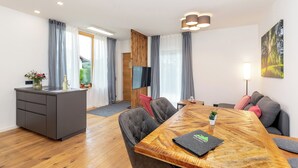A modern living room with a wooden dining table, grey sofa, and a TV mounted on the wall. - MyWinkl-Design-Ferienwohnungen  (Reit im Winkl)