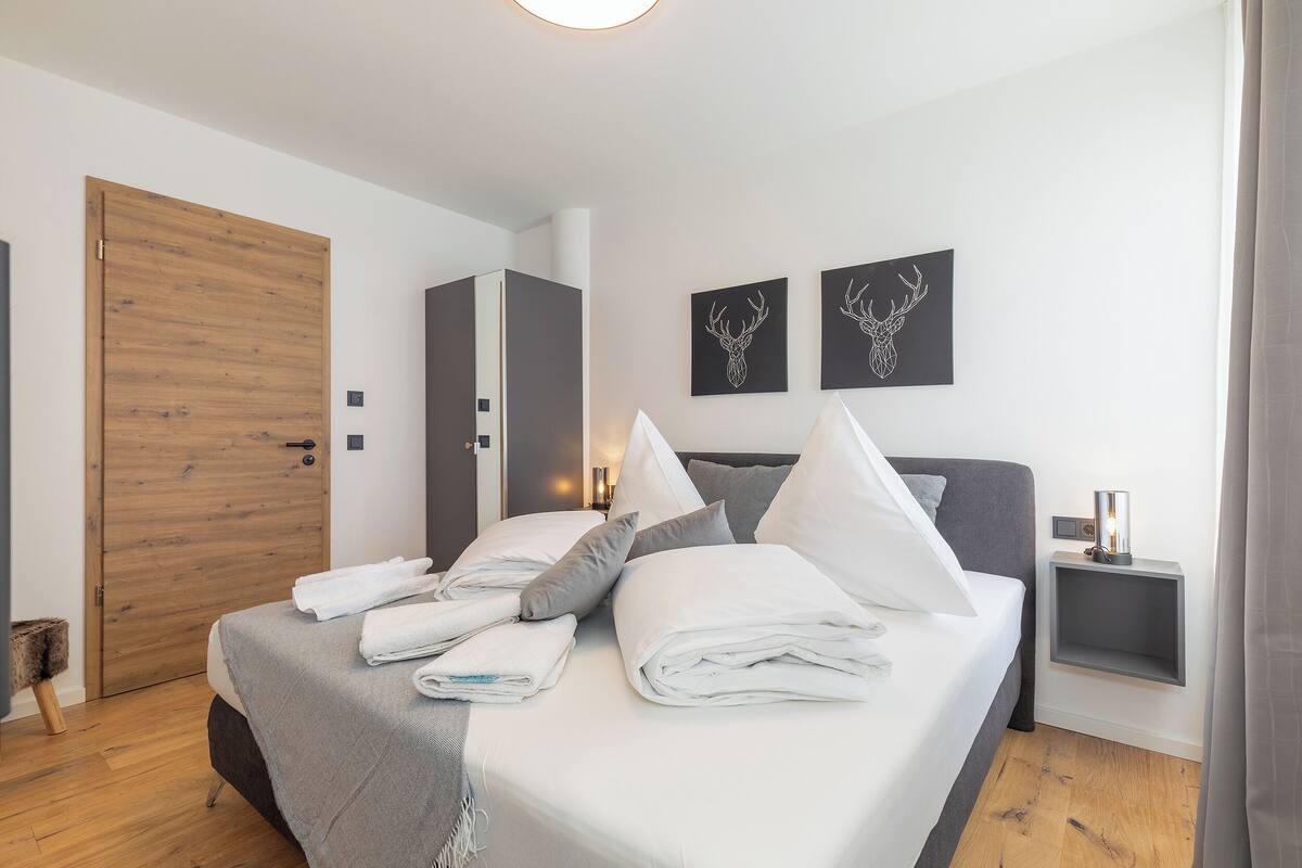 A neatly made bed with white linens, a grey headboard, and two wall-mounted deer head decorations.