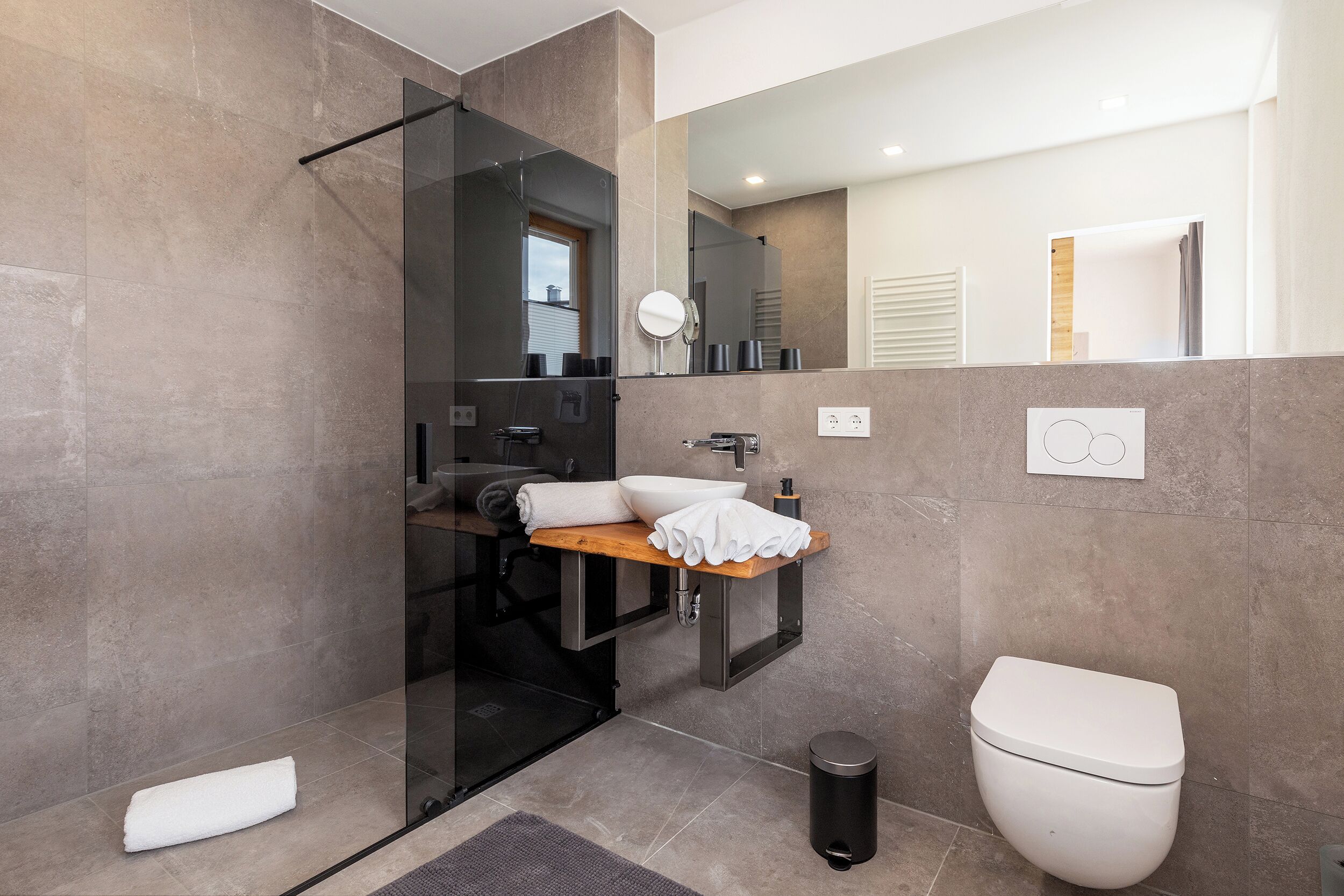 Un baño moderno con cabina de ducha de vidrio, tocador de madera, inodoro y espejo.