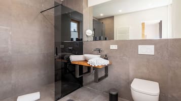 Un baño moderno con cabina de ducha de vidrio, tocador de madera, inodoro y espejo.