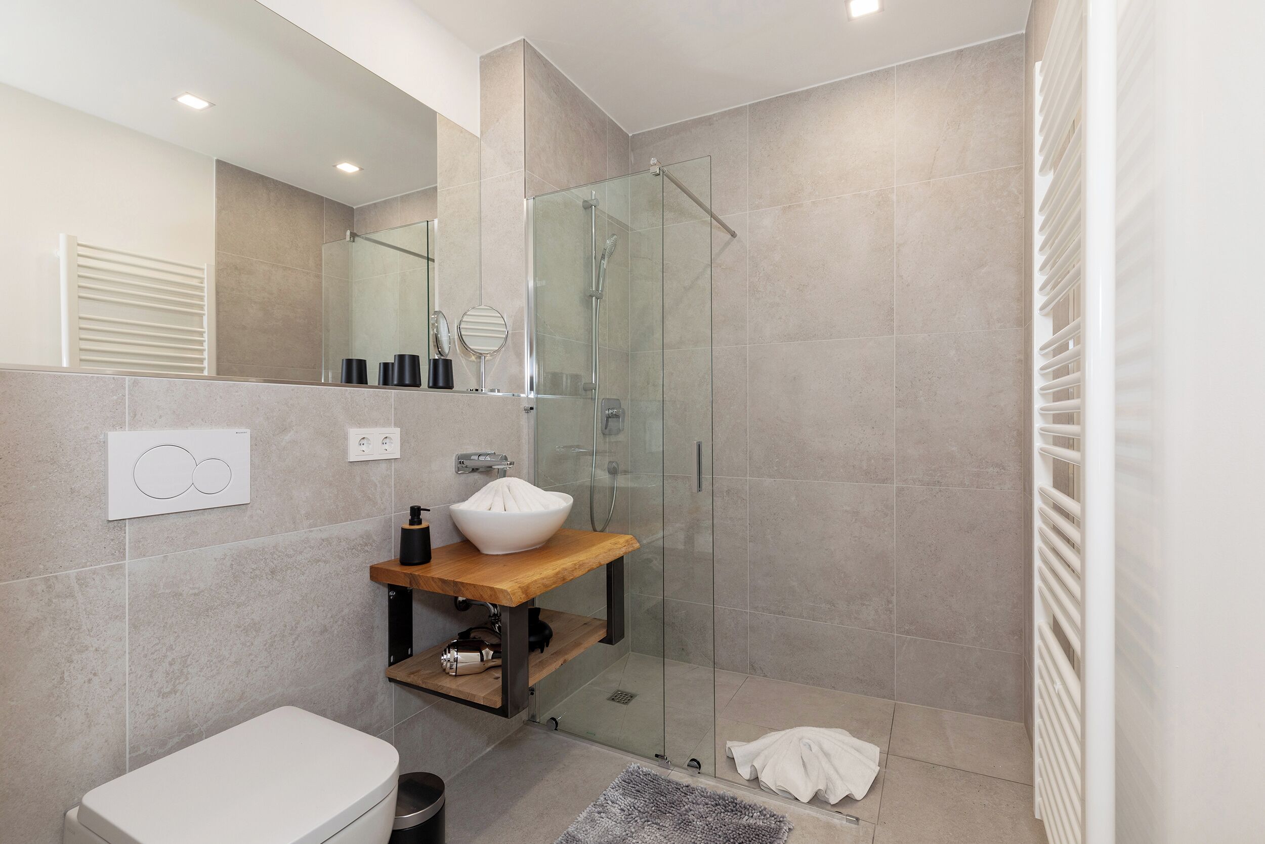 Un baño moderno con ducha de vidrio, un lavamanos blanco y un mueble de tocador de madera.