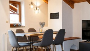 A dining area with a wooden table, four chairs, a TV, and pendant lights. - MyWinkl-Design-Ferienwohnungen  (Reit im Winkl)