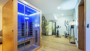 A sauna with a wooden exterior and glass doors, a wooden floor, and exercise equipment in the background. - MyWinkl-Design-Ferienwohnungen  (Reit im Winkl)