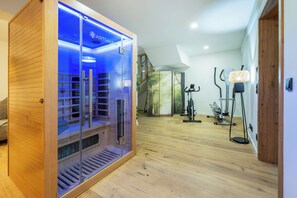A sauna with a wooden exterior and glass doors, a wooden floor, and exercise equipment in the background. - MyWinkl-Design-Ferienwohnungen  (Reit im Winkl)