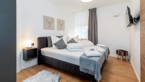 A modern bedroom with a bed, bedside tables, a small stool, and artwork on the wall. - MyWinkl-Design-Ferienwohnungen  (Reit im Winkl)