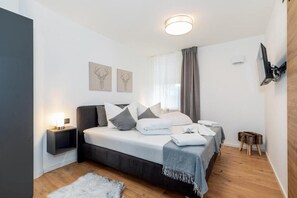 A modern bedroom with a bed, bedside tables, a small stool, and artwork on the wall. - MyWinkl-Design-Ferienwohnungen  (Reit im Winkl)