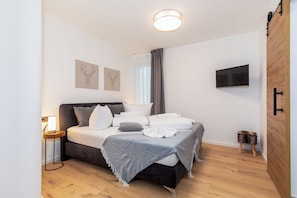 Quarto moderno com cama, mesa de cabeceira e televisão na parede.