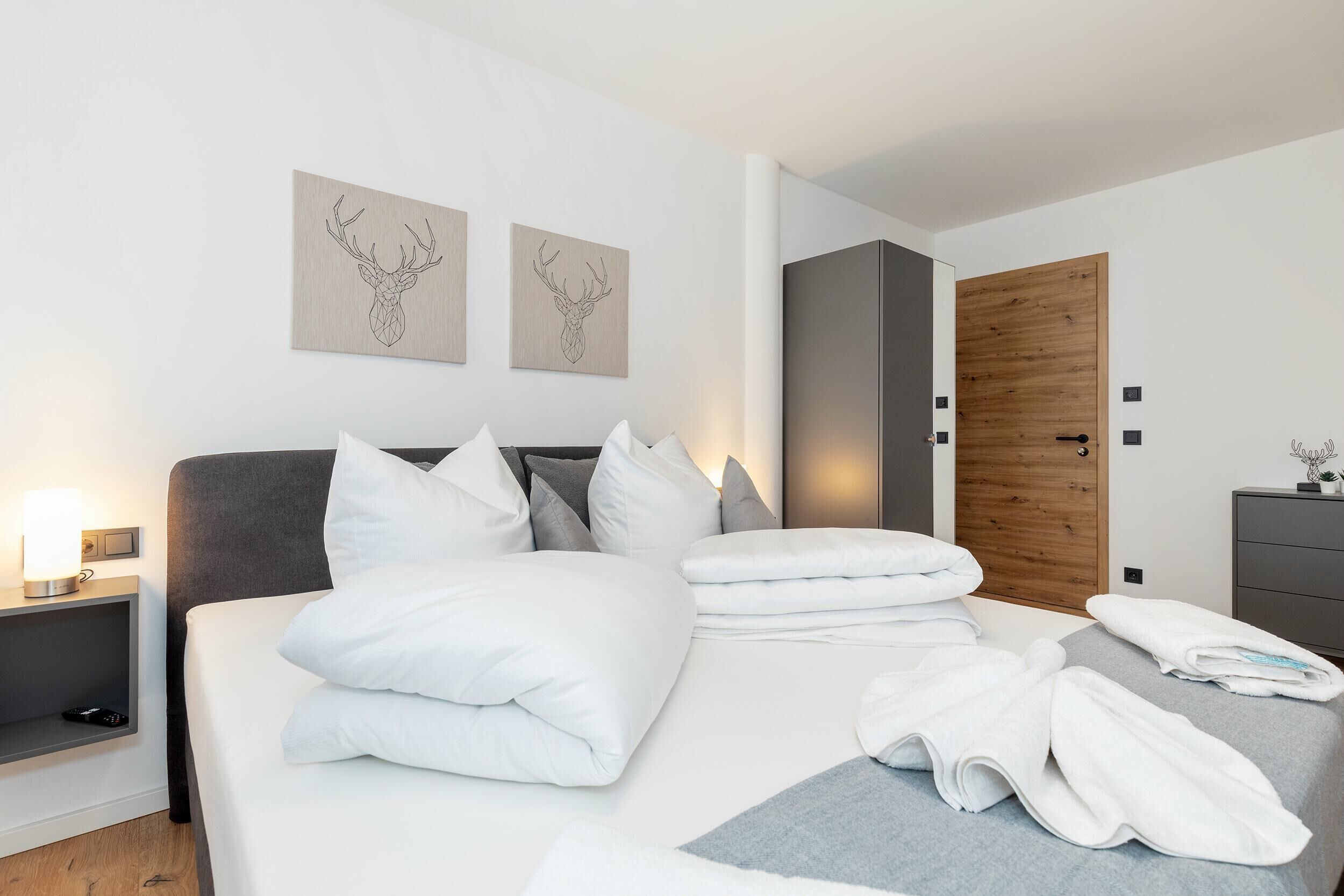 A modern hotel room with a neatly made bed, a wooden door, and two wall-mounted artwork.